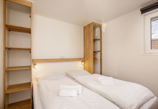 Chambre avec deux lits simples, draps blancs, serviettes et étagères au Chalet Comfort 4, Hunzepark.