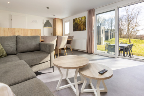 Sala luminosa en el Chalet Comfort 6 de Hunzepark, Países Bajos, con sofá, mesas y vista al jardín.