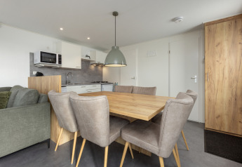 Moderne spisestue og køkken i Chalet Comfort 6 ved Hunzepark, Nederlandene med seks stole og træbord.
