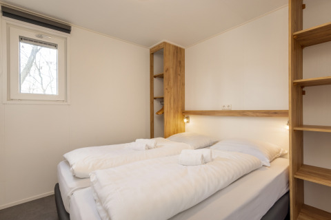 Chambre moderne avec lit double, étagères en bois et murs clairs au Chalet Comfort 6 du Hunzepark, Pays-Bas.