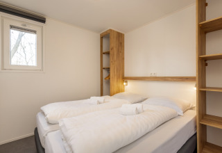 Dormitorio moderno con cama doble, estantes de madera y paredes blancas en Chalet Comfort 6 de Hunzepark, Países Bajos.