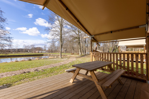 Vue depuis une tente safari au Hunzepark aux Pays-Bas avec table de pique-nique, terrasse et étang.