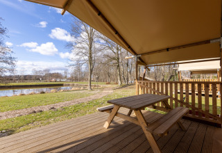 View from Safari tent 6 at Hunzepark in the Netherlands with a picnic table, deck, and pond outside.