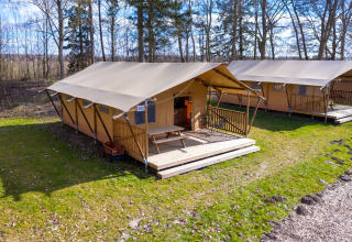 La tienda Safari 6 en Hunzepark, Países Bajos, con terraza de madera y banco exterior en la naturaleza.