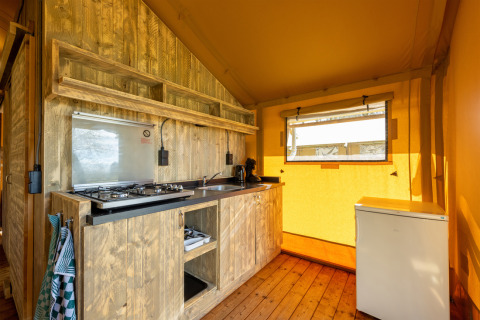 Intérieur de la tente safari 6 à Hunzepark, Pays-Bas, avec cuisine en bois et petit frigo.