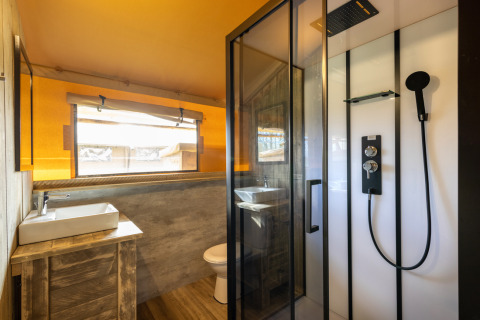 Salle de bain de la tente Safari 6 à Hunzepark aux Pays-Bas, moderne avec douche, lavabo et fenêtre large.