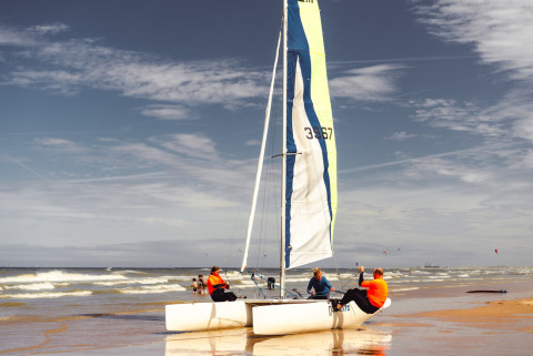 Personas preparan un catamarán en la playa cerca de Callantsoog, Países Bajos, bajo cielo parcialmente nublado.
