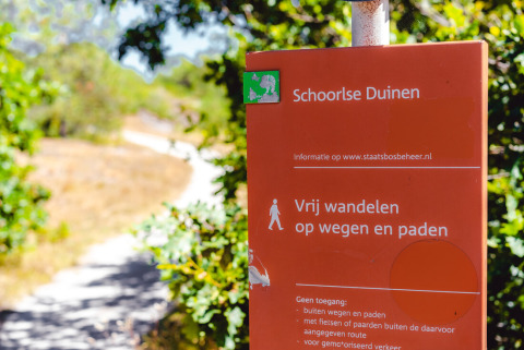 Cartel rojo del área natural Schoorlse Duinen cerca de Callantsoog, Países Bajos, junto a un sendero soleado.