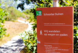 Rødt skilt for Schoorlse Duinen naturreservat nær Callantsoog, Holland, omgivet af grønne træer.