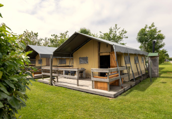 Buitenaanzicht van Safaritent 4 met houten veranda, groene grasmat en andere tenten op de achtergrond.