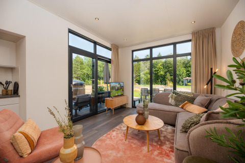 Helles Wohnzimmer im Cannenburch Deluxe Lodge bei de Bosgraaf, Niederlande, mit großer Fensterfront zum Garten.