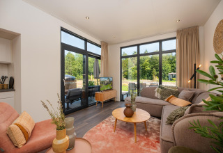 Lichte, moderne woonkamer in het Cannenburch Deluxe lodge bij de Bosgraaf, Nederland, met grote ramen en uitzicht.