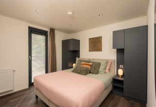 Moderne slaapkamer in de Cannenburch Deluxe-lodge bij de Bosgraaf, Nederland, met een tweepersoonsbed en sfeervol interieur.