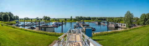 Panoramic view of a marina at a glamping accommodation, with boats and lush green surroundings under blue sky.