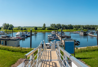 Panoramic view of a marina at a glamping accommodation, with boats and lush green surroundings under blue sky.