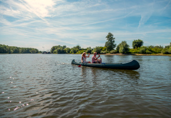 Tre persone remano in canoa su un lago tranquillo durante una vacanza glamping immersi nella natura.