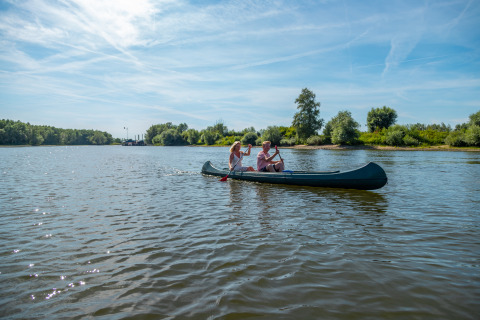 Three people canoeing on a calm lake under a blue sky during a glamping getaway in a natural setting.