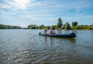 Tre persone remano in canoa su un lago tranquillo durante una vacanza glamping immersi nella natura.