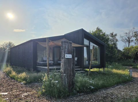 Baita moderna in legno scuro presso Slowlodge 2 con il cartello 'Rise', immersa nella natura.
