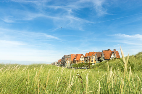 Ferienhäuser mit roten Dächern im Breeduyn Village, Westflandern, Belgien, mit Dünen und Himmel.