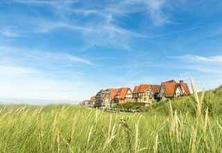Ferienhäuser mit roten Dächern im Breeduyn Village, Westflandern, Belgien, mit Dünen und Himmel.