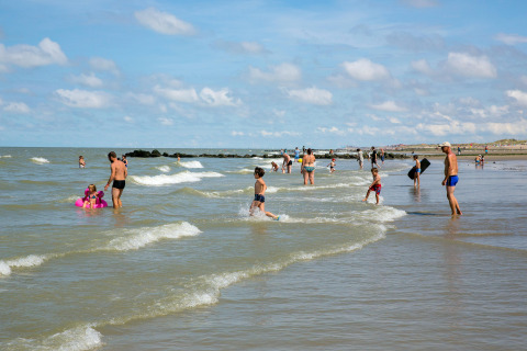 Menschen genießen einen sonnigen Tag am Strand bei Bredene in Belgien, schwimmen und spielen im Wasser.