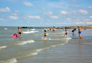 Menschen genießen einen sonnigen Tag am Strand bei Bredene in Belgien, schwimmen und spielen im Wasser.