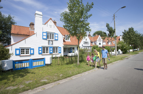 Familie spaziert an malerischen weißen Häusern mit roten Dächern in Bredene, Westflandern, Belgien vorbei.