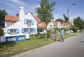 Familie spaziert an malerischen weißen Häusern mit roten Dächern in Bredene, Westflandern, Belgien vorbei.