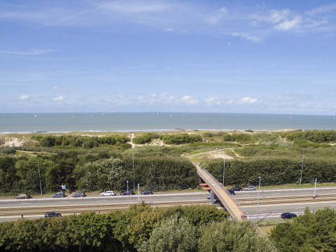 Blick auf Straßen, Eisenbahn, grüne Dünen und Meer nahe Bredene, Belgien, unter blauem Himmel.