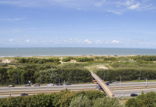 Blick auf Straßen, Eisenbahn, grüne Dünen und Meer nahe Bredene, Belgien, unter blauem Himmel.