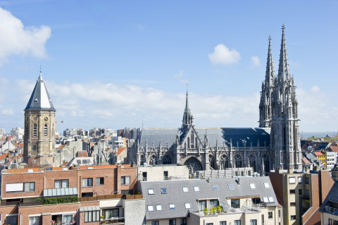 Blick auf Bredene, Belgien mit einer gotischen Kirche und modernen Gebäuden unter blauem Himmel.