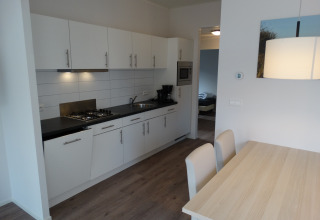 Moderne køkken og spiseplads i Lodge 4 på Breeduyn Village, Belgien, med hvide skabe og træbord.