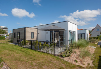 Lodge 4 moderna con terraza y verja negra, rodeada de vegetación bajo un cielo azul con nubes.
