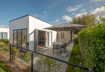 Lodge 6 natuurhuisje met terras, tuintafel en parasol in een groene omgeving onder een blauwe hemel.