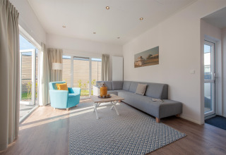 Lyst og moderne opholdsstue i Lodge 6 på Breeduyn Village, Belgien, med store vinduer og stilfuld indretning.