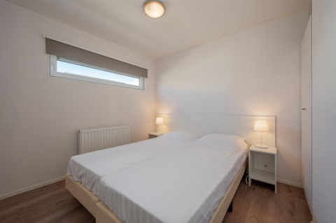 Schlafzimmer der Lodge 6 im Breeduyn Village, Belgien, mit Doppelbett, Nachttischen und moderner Einrichtung.