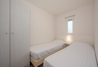 Schlichtes Schlafzimmer mit zwei Einzelbetten, Nachttisch und Kleiderschrank in Lodge 6, Breeduyn Village, Belgien.