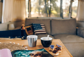 Intérieur d'une tiny house Airstream avec une table, café, encas et magazine dans une ambiance cosy.