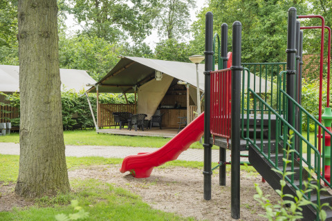 Legeplads og glampingtelt på Camping de Haer i Overijssel, Holland, omgivet af grønne træer og græs.