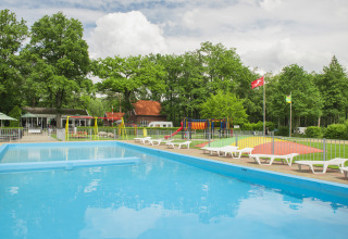 Buitenzwembad en kleurrijke speeltuin bij Camping de Haer in Overijssel, omgeven door bomen en ligstoelen.