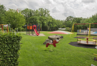 Speeltuin bij Camping de Haer in Overijssel met rode glijbaan, schommels en springkussen.