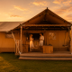 Ein luxuriöses Glamping-Zelt bei Sonnenuntergang, in dem zwei Personen auf einer Holzterrasse entspannen.