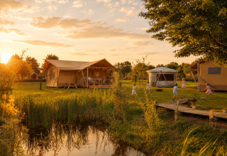 Glampingtent op Holiday park Eigen Wijze in Nederland bij zonsondergang, kinderen spelen buiten.