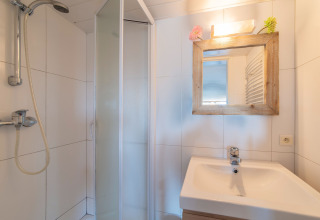 Bagno luminoso a Le Chalet sous les Hetres in Belgio con doccia, lavandino e specchio con cornice in legno.