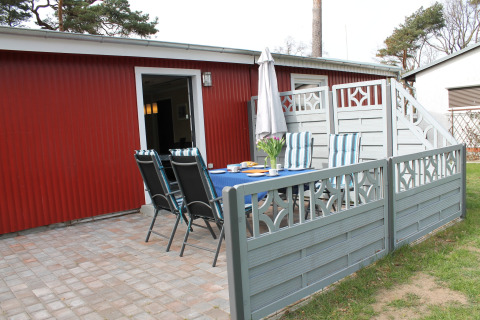 Buitenterras aan lodge 'On the Beach' in Duitsland, met tafel, stoelen en rood gebouw op de achtergrond.