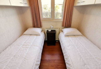 Et simpelt soveværelse med to enkeltsenge, hvide dyner, natbord og vindue i Chalet Basic, De Woudhoeve.