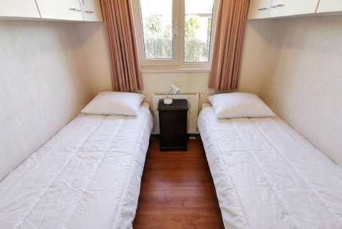 Eenvoudige slaapkamer met twee eenpersoonsbedden, witte dekbedovertrekken in Chalet Basic, De Woudhoeve.