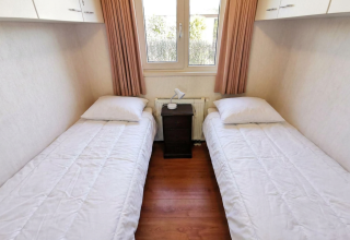Eenvoudige slaapkamer met twee eenpersoonsbedden, witte dekbedovertrekken in Chalet Basic, De Woudhoeve.