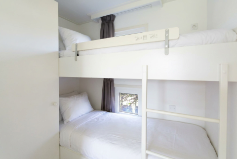 Lichte kamer met stapelbed en witte lakens in Chalet Basic bij De Woudhoeve, Nederland, met klein raam.